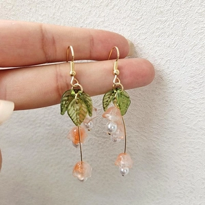 Close-up of pink bellflower earrings with green leaves and white pearls details