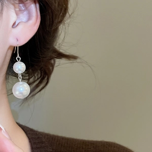 Close-up of elegant double pearl earrings with silver hooks worn by a woman
