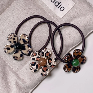 Three leopard print flower hair ties with rhinestones and beads on grey canvas background