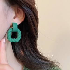 Detail shot of model wearing green geometric resin earrings with twisted drop charms