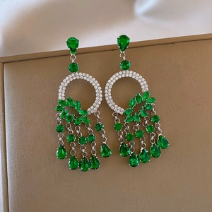 Detail of silver drop earrings featuring green teardrop stones and sparkling tassels