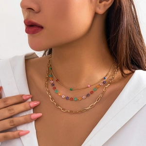Close-up of layered gold chains with colorful enamel flowers and beads on a model
