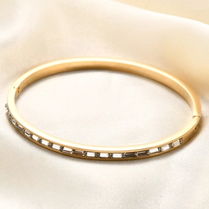 Vista detallada de un brazalete ovalado dorado con circonitas baguette sobre fondo seda