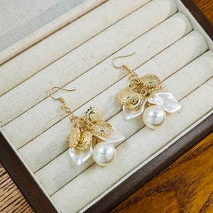 Detail of gold hook earrings featuring white flower petals and sun embossed discs
