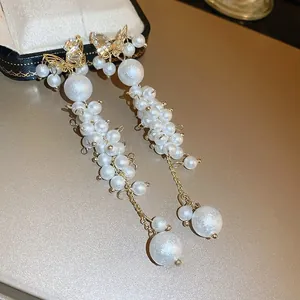 Detail of long butterfly tassel earrings with white pearls and gold sparkling accents