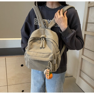 Detail of beige corduroy backpack showing textured fabric and creative persimmon pendant