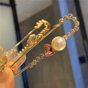 Detailed macro view of a gold-plated safety pin with pearl and heart crystal accents