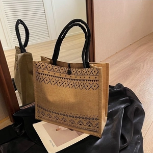 Detail of linen tote bag with black geometric patterns and woven handles on silk