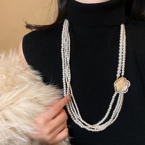 Detail of a multi-layer pearl necklace with a white camellia flower pendant on a model