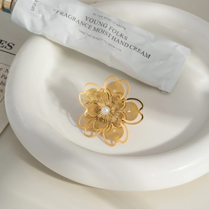 Hollow camellia flower ring in 18K gold finish with center pearl on white ceramic plate