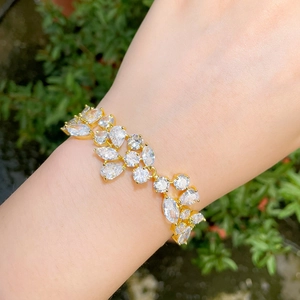 Detail of a sparkling gold bracelet with cubic zirconia worn against a green background
