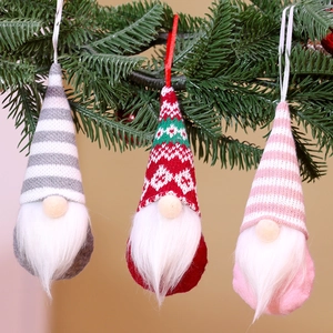 Detailed view of three knitted faceless Christmas gnomes hanging on a festive pine tree branch