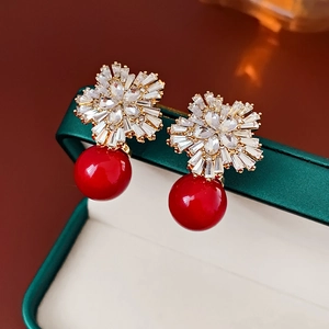 Luxuriöse goldene Blumenohrringe mit Kristallen und roten Perlen auf einer Schmuckschatulle