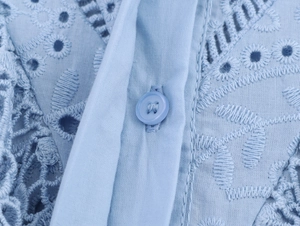 Dettaglio del tessuto ricamato traforato azzurro e bottone coordinato su una camicia casual