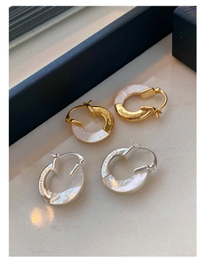 Macro detail of gold and silver hoop earrings with mother of pearl and Confession engraving
