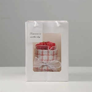 Detail of a red soap rose bouquet inside a white paper gift bag with a clear window