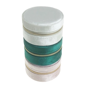 Vertical stack of three velvet travel jewelry cases in grey, emerald green, and light pink