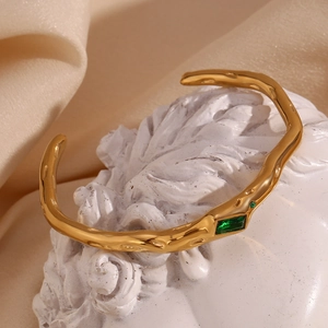 Macro detail of 18K gold plated open cuff bracelet with emerald green zircon stone