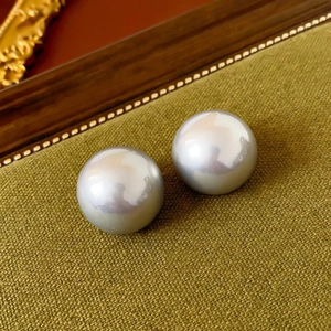 Macro shot of polished round pearl earrings on green fabric with vintage wooden frame