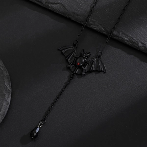 Gothic black bat necklace with red ruby eye and drop pendant on a dark stone background