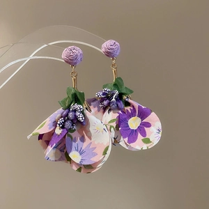 Detailed macro shot of handmade purple fabric flower earrings with green leaves and beads