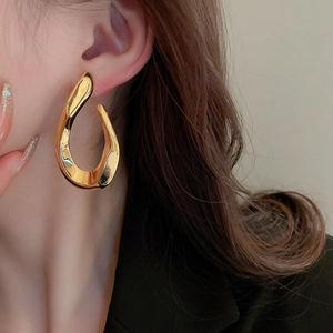 Close-up of a gold twisted irregular fluid metal earring worn by a female model