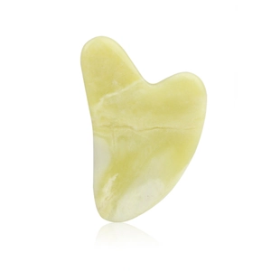 Macro shot of heart-shaped jade gua sha board with smooth texture and pale yellow finish