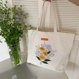 Detail view of floral embroidery on a white canvas tote bag with a woven brand label