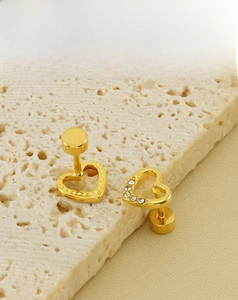 Detail view of heart-shaped gold stud earrings with rhinestones on a beige stone base