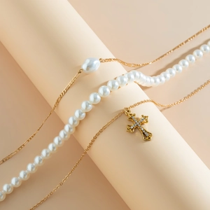 Detailed macro view of layered beaded necklace with pearls, gold chain, and rhinestone cross