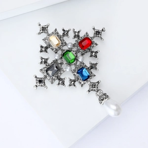 Macro view of vintage baroque silver cross brooch with colorful gems and pearl pendant