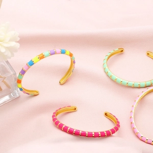 Detail of colorful enamel cuff bracelets in rainbow, mint, and pink over golden base