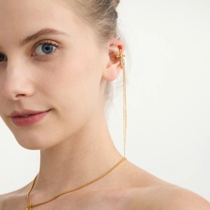 Detailed view of a gold cross ear cuff with tassel chains and matching necklace on a model