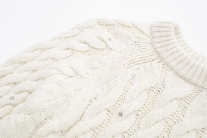 Detailaufnahme des Rundhals-Zopfstrickpullovers mit funkelnden Strasssteinen
