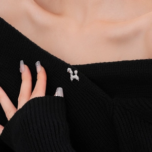 Close-up of a silver poodle brooch with zircons pinned on a black knitted sweater
