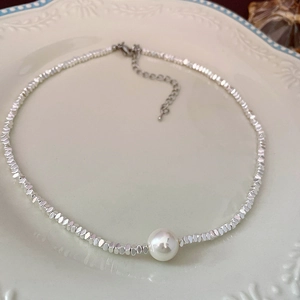 Detailed macro of a beaded necklace with silver-toned faceted beads and a single white pearl