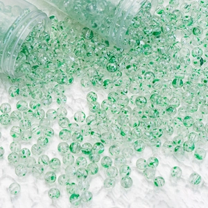 Close-up of clear glass beads with green floral patterns spilling from a tube