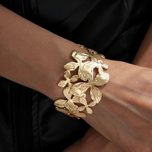 Detailed macro view of wide gold metal open cuff bracelet with floral cutout patterns