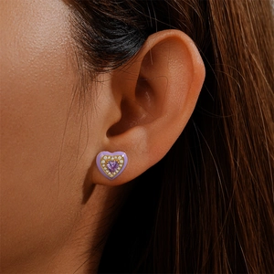Close-up of heart-shaped earring with purple enamel and diamonds worn on a model's ear