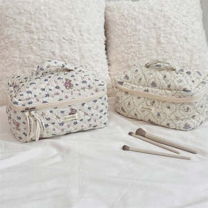 Detailed view of quilted beige makeup bags with bear patterns on a soft white bed