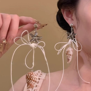 Detail of seashell and starfish fringe earrings with white rope bows on female model