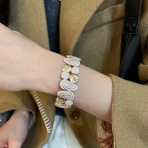 Close-up of a wide vintage gold-tone bracelet with white enamel spirals and rhinestones