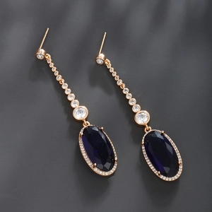Macro shot of long gold earrings with deep blue oval gemstones and sparkling white zircons