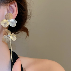 Detailed shot of golden flower earrings with brushed metal petals and long tassels on a model