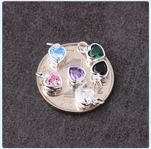 Macro shot of colorful heart-shaped cubic zirconia pendants next to a coin for size