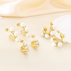 Elegant C-shaped gold earrings with white pearls on a luxury silk and ceramic background