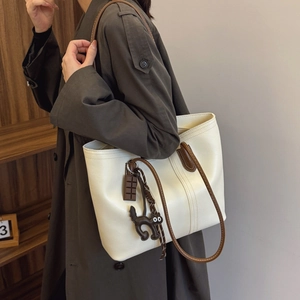 Chic beige tote bag with brown straps and cute cat charms shown in a lifestyle side view
