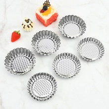 Close-up of seven silver fluted tart molds with perforated bases on marble background