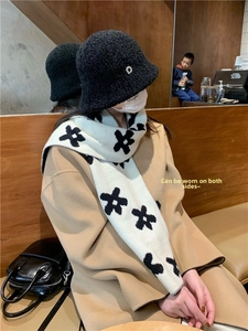 Detail of a thick knitted scarf with black flower patterns and a black plush bucket hat