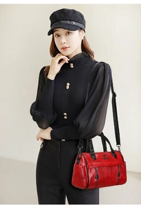 Detail of a red leather crossbody bag with gold hardware styled with a black outfit
